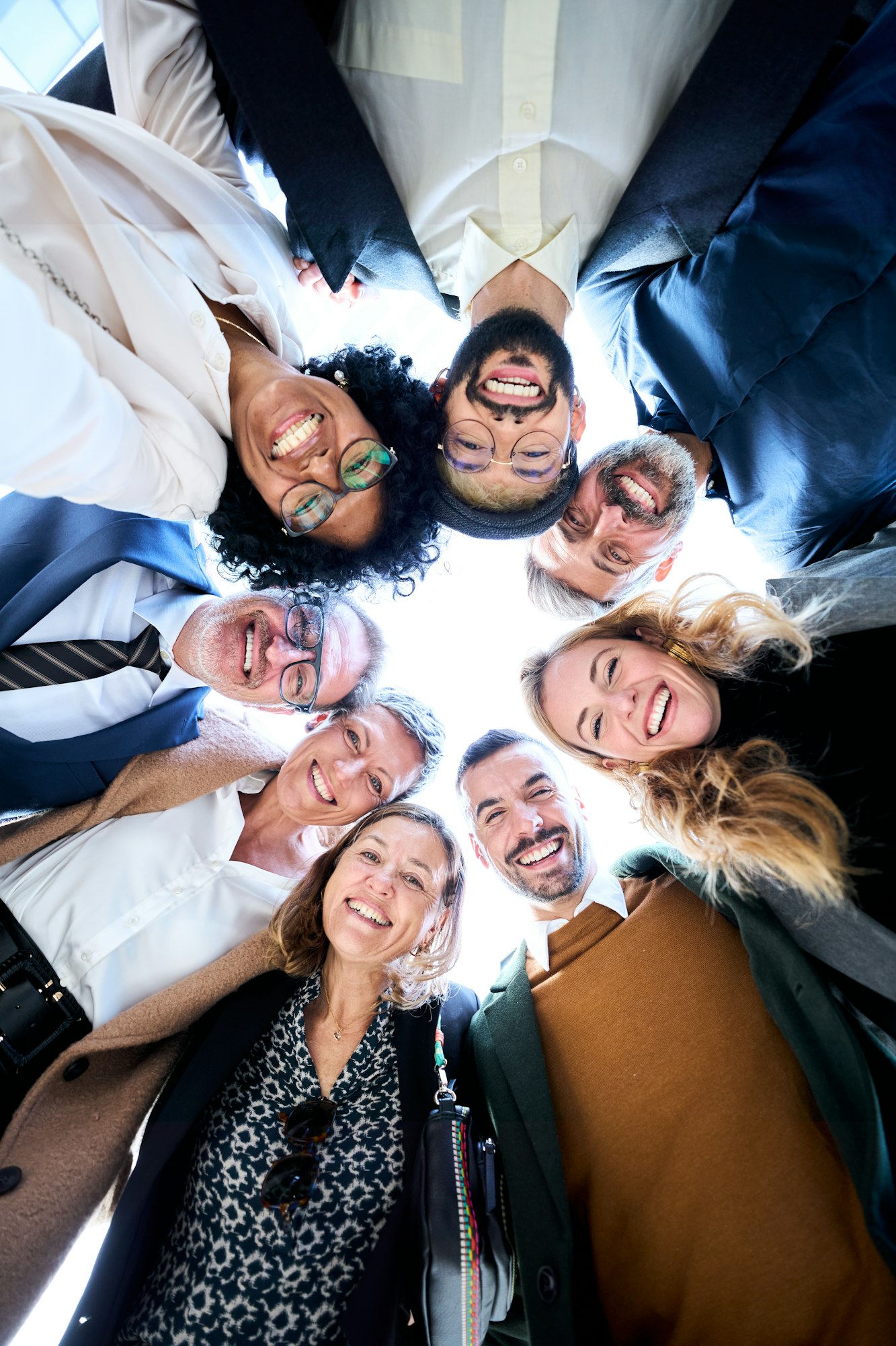 A group of diverse business people in formal wear gathered in a circle smiling and stacking hands